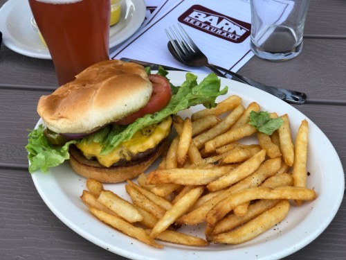 A cheeseburger with lettuce, tomato, and onion, served with a side of golden fries and a drink in the background.