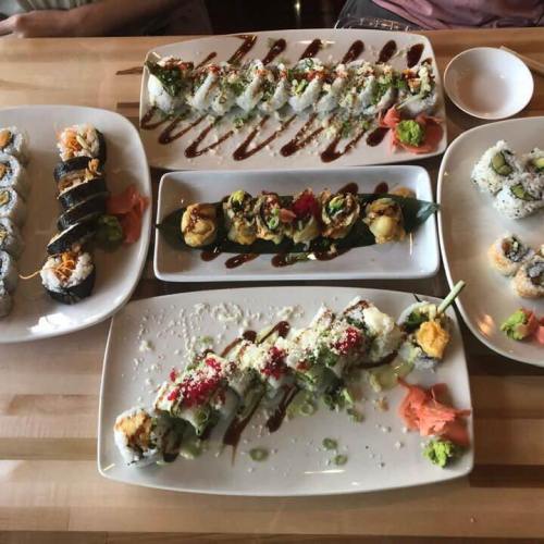 A variety of sushi rolls and sashimi arranged on plates, garnished with wasabi and pickled ginger.