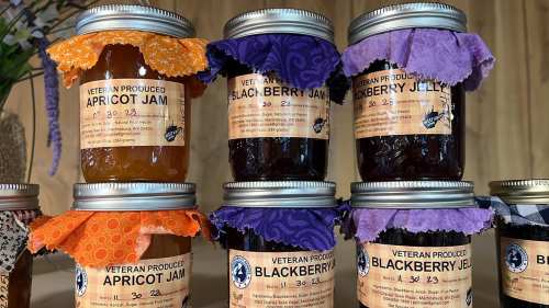 Jars of apricot jam, blackberry jam, and blackberry jelly, each labeled "Veteran Produced" with colorful fabric tops.