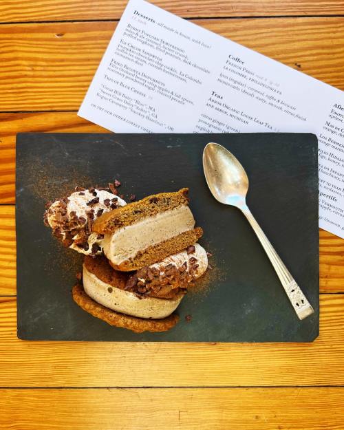 A dessert plate featuring two ice cream sandwiches with chocolate chips, accompanied by a spoon and a menu in the background.