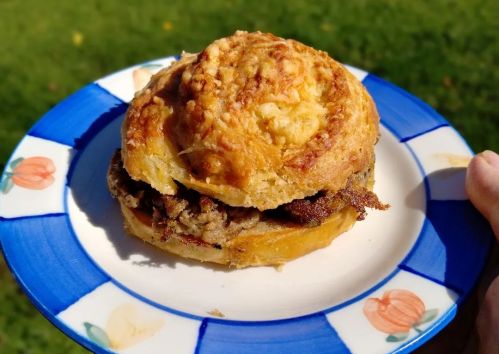 A close-up of a savory sandwich on a decorative plate, held in a hand, with green grass in the background.