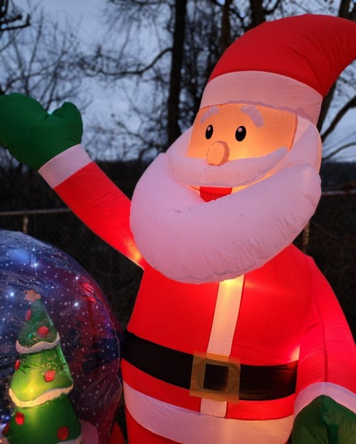 A large inflatable Santa Claus waving, with a glowing Christmas tree in a snow globe nearby.