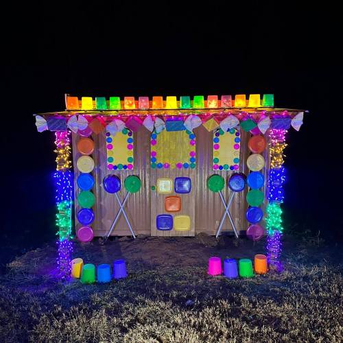 A brightly lit outdoor structure decorated with colorful cups, plates, and lights against a dark background.