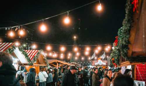 A bustling night market filled with people, festive lights, and decorated stalls, creating a warm holiday atmosphere.