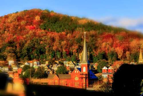 A scenic view of a town with colorful autumn foliage and a prominent church steeple against a hillside.