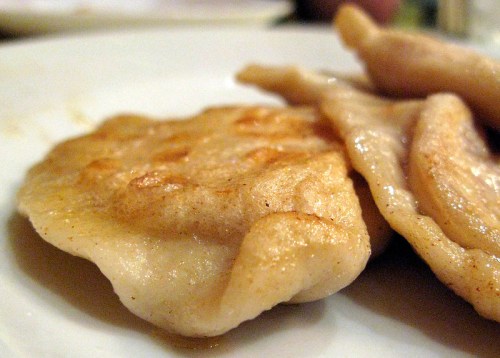 Close-up of golden-brown dumplings on a white plate, showcasing a crispy texture and soft edges.