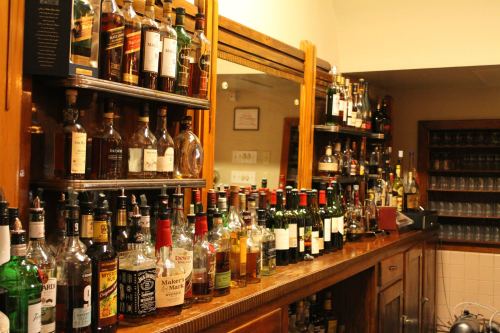 A wooden bar lined with various bottles of liquor, including whiskey, wine, and spirits, reflecting a cozy atmosphere.