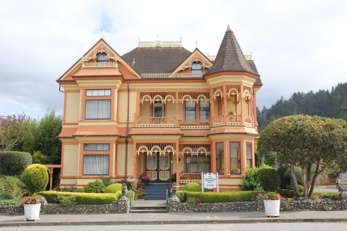 A large, ornate Victorian-style house with colorful trim, intricate details, and well-maintained gardens.