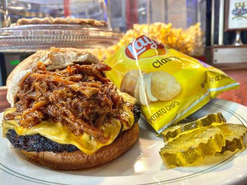 A plate featuring a cheesy pulled pork sandwich, Lay's potato chips, and pickles on the side.