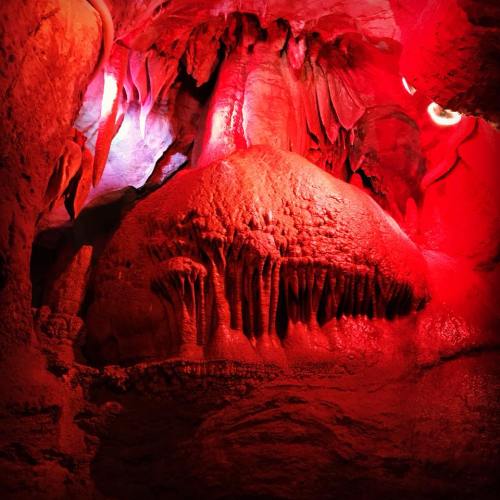 A cave interior featuring a large, textured rock formation illuminated by red lighting.