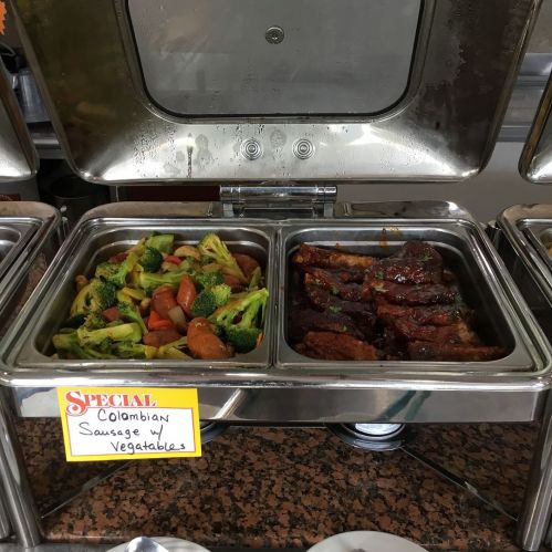 A buffet tray with Colombian sausage and vegetables, featuring broccoli and carrots, labeled as a special dish.