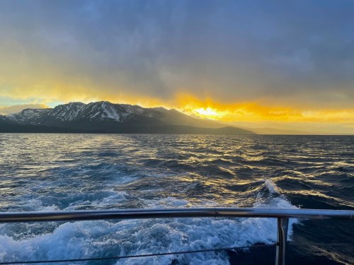 A scenic view of mountains at sunset, with waves in the foreground and a colorful sky reflecting on the water.