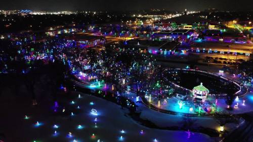 Aerial view of a vibrant holiday light display in a park, with colorful lights illuminating the snow and surrounding area.