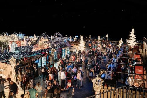 A bustling holiday market illuminated with colorful lights, featuring crowds enjoying festive decorations and activities.