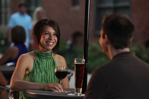 A woman in a green top smiles at a man while enjoying drinks at an outdoor café.