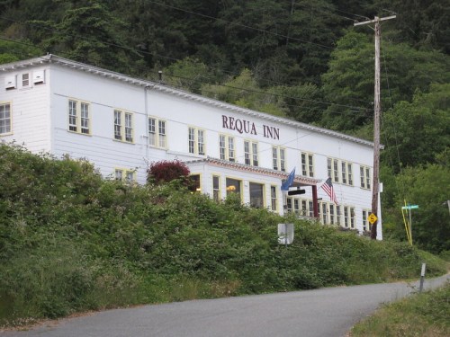 A white building with "Requa Inn" sign, surrounded by greenery, located near a road with power lines in the background.