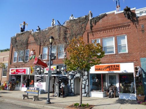 A Halloween store with spooky decorations, skeletons, and figures on the roof, set in a brick building.