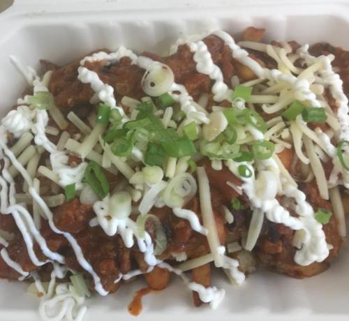 A takeout container filled with pasta topped with meat sauce, shredded cheese, green onions, and drizzled with white sauce.