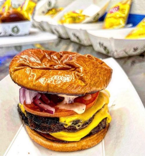 A close-up of a juicy cheeseburger with melted cheese, tomatoes, onions, and a toasted bun on a white tray.