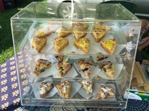 A clear display case filled with assorted triangular pastries, including savory and sweet varieties, on a patterned tablecloth.