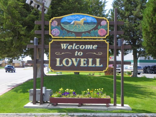 Welcome sign for Lovell, featuring a horse and flowers, surrounded by greenery and a clear blue sky.