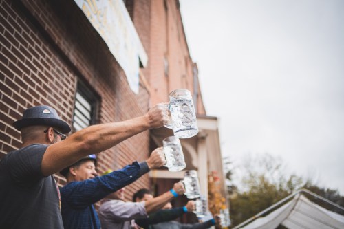 A group of people raising large beer mugs outdoors, celebrating at a festive event.