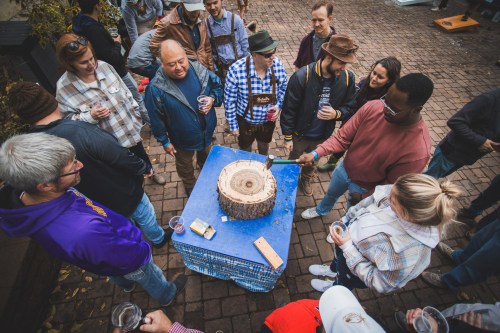 A group of people gathered around a wooden stump, enjoying drinks and socializing outdoors.