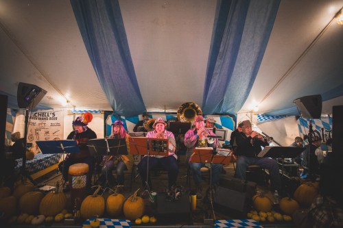 A band performs under a tent decorated with blue and white fabric, surrounded by pumpkins and festive decor.