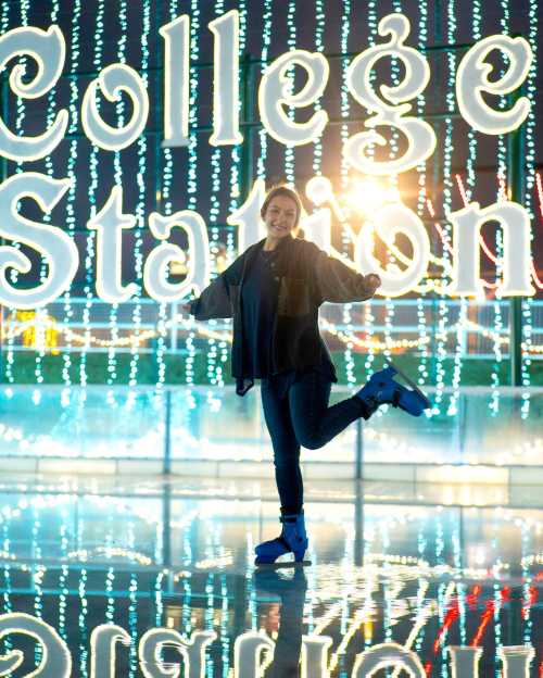 A person ice skating in front of a brightly lit "College Station" sign at night.