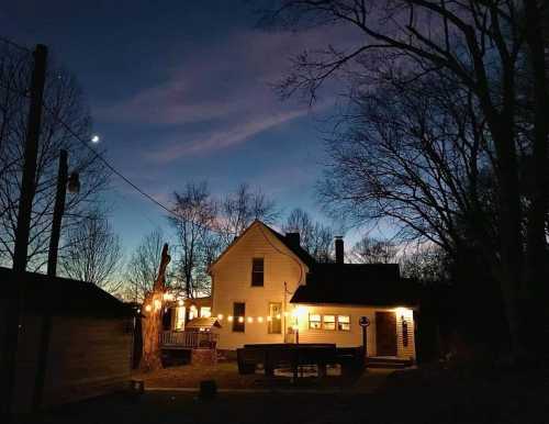 A cozy house illuminated at dusk, surrounded by trees and a clear sky with a crescent moon.