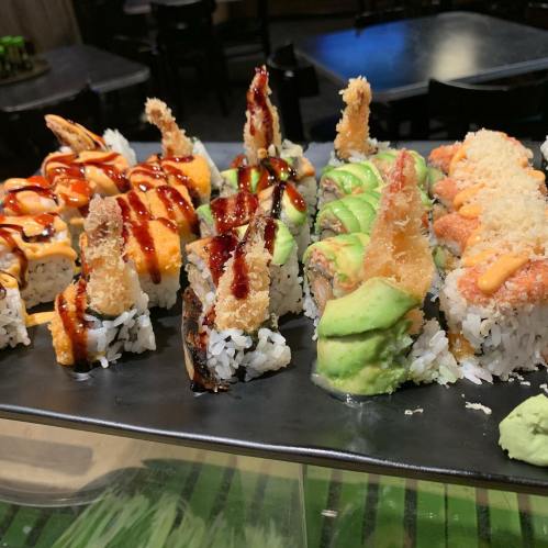 A platter of assorted sushi rolls, featuring shrimp tempura, avocado, and various sauces, on a black serving tray.