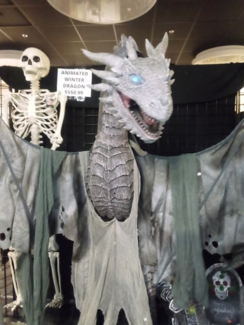 A large animated winter dragon display with a skeleton in the background, set against a dark backdrop.