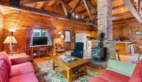 Cozy wooden cabin interior with a living area, kitchen, and a wood stove, featuring rustic decor and warm lighting.