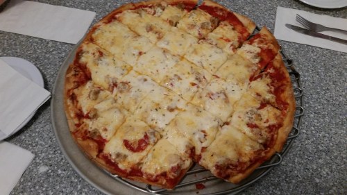 A round pizza with a golden crust, topped with melted cheese and tomato sauce, cut into square slices.