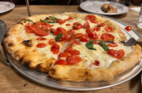 A freshly baked pizza topped with melted cheese, cherry tomatoes, and fresh basil on a metal tray.