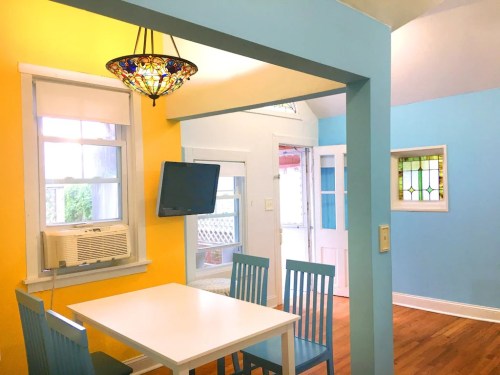 Brightly colored dining area with yellow and blue walls, a white table, blue chairs, and a stained glass window.