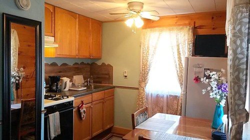 Cozy kitchen with wooden cabinets, a dining table, and a window with sheer curtains, featuring a ceiling fan and appliances.