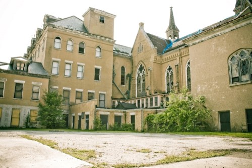 Abandoned building with Gothic architecture, overgrown vegetation, and a clear sky in the background.