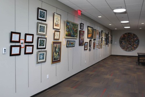 A gallery wall displaying various framed artworks and informational plaques in a well-lit hallway.