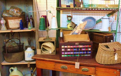 A vintage display featuring spools of thread, glass bottles, and various antique items on shelves and a wooden table.
