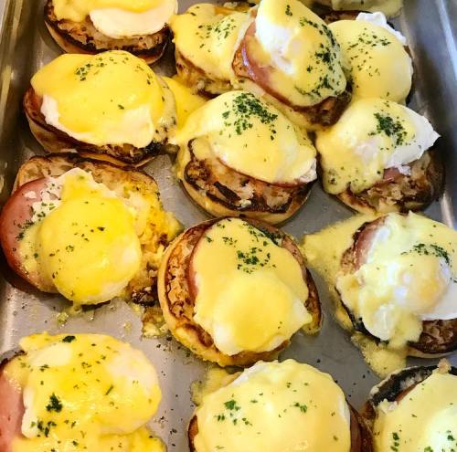 A tray of eggs Benedict with poached eggs, ham, and melted cheese, garnished with parsley.