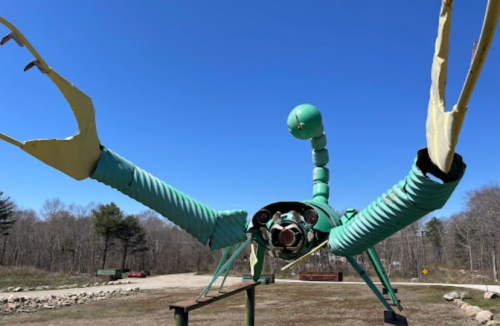 A large, whimsical sculpture of a crab made from metal and pipes, set against a clear blue sky.