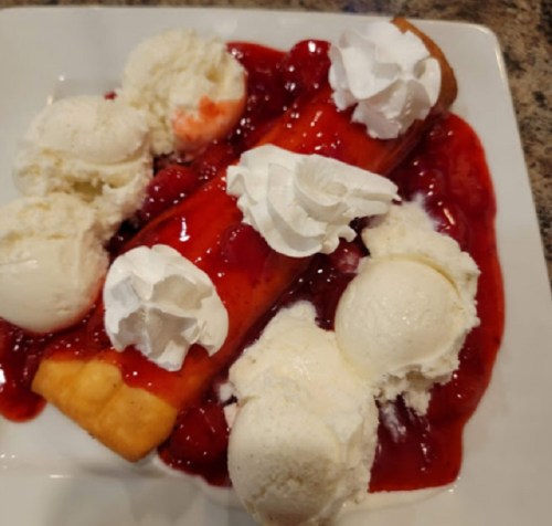 A dessert plate featuring a rolled pastry topped with cherry sauce and whipped cream, surrounded by scoops of vanilla ice cream.