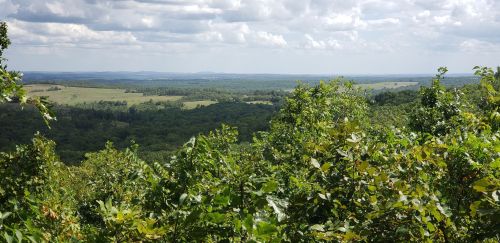 A panoramic view of rolling green hills and valleys under a partly cloudy sky.