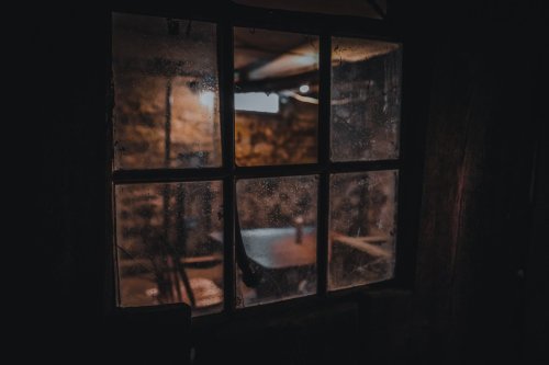 A dimly lit room seen through a dusty window, with a table and chairs visible inside.