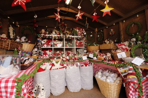 A cozy holiday market stall filled with festive decorations, plush toys, and seasonal crafts in baskets and bags.