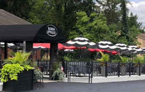 Outdoor dining area with black and white striped umbrellas, greenery, and a sign for "Mamma Spriggs."