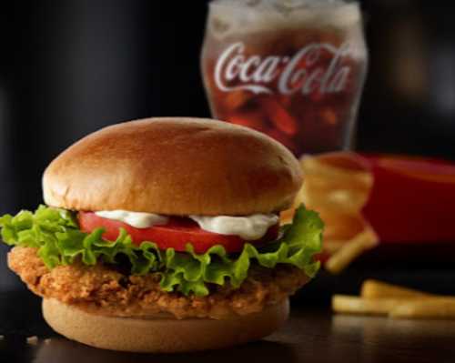 A crispy chicken sandwich with lettuce, tomato, and mayo, served with fries and a glass of Coca-Cola in the background.