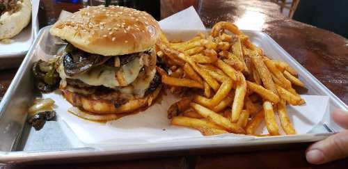 A sesame seed bun burger with melted cheese, grilled onions, and jalapeños, served with a side of crispy fries.