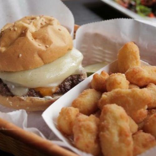 A juicy cheeseburger with melted cheese on a sesame seed bun, served with a side of crispy golden tater tots.